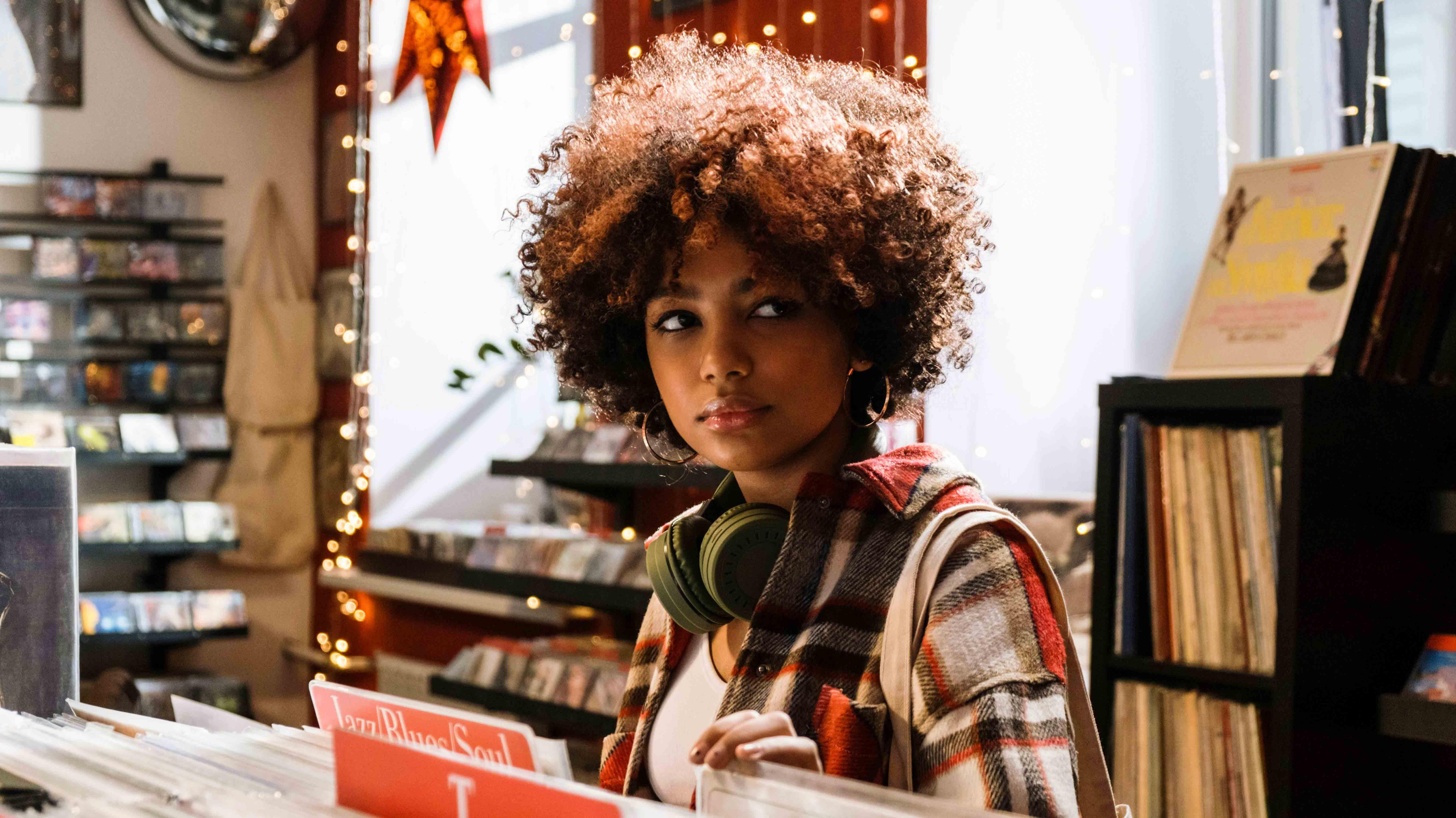 Woman browsing vinyl records with wireless headphones around neck in cozy music store