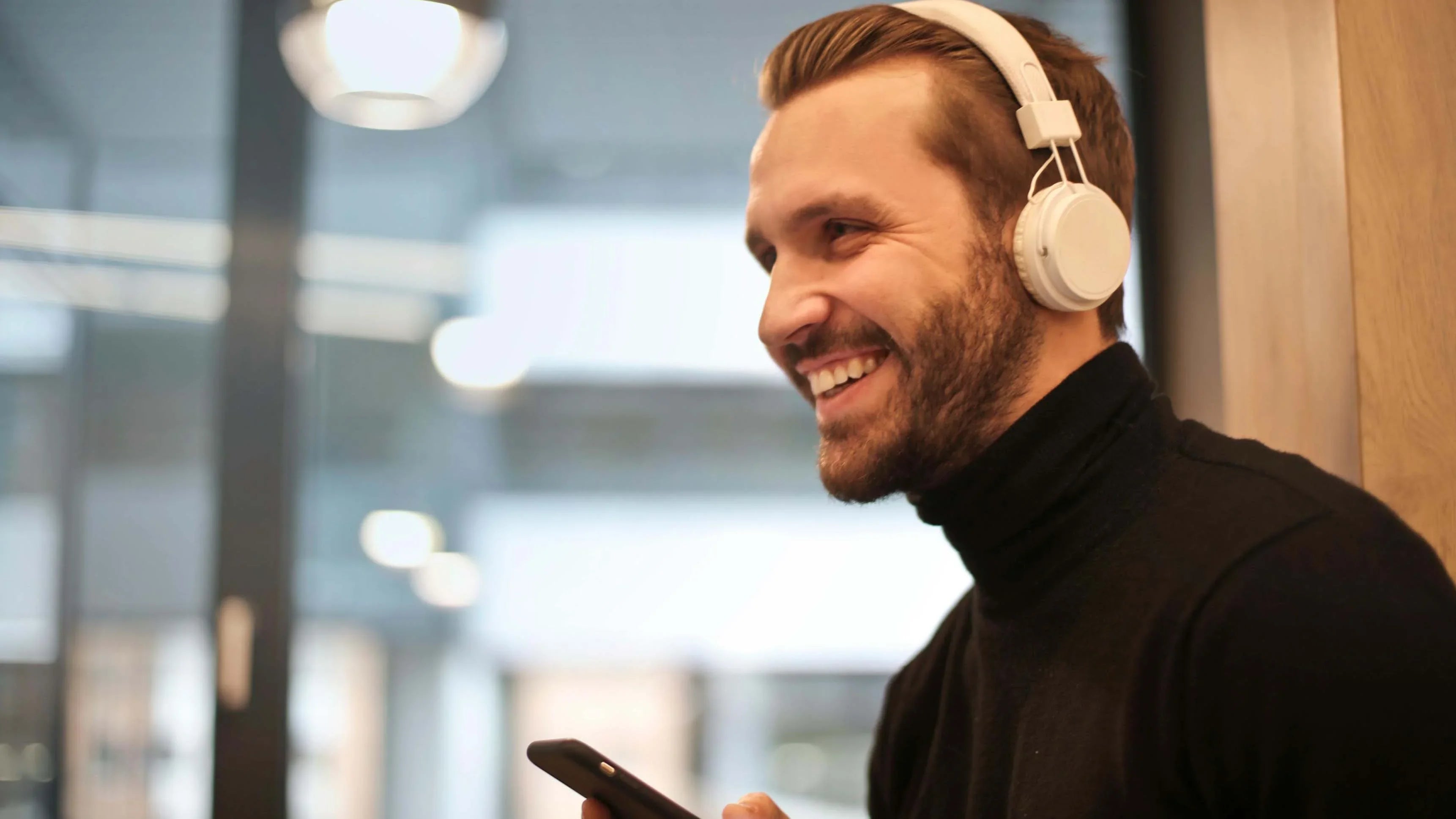 Man smiling with white wireless headphones, using smartphone for immersive audio experience