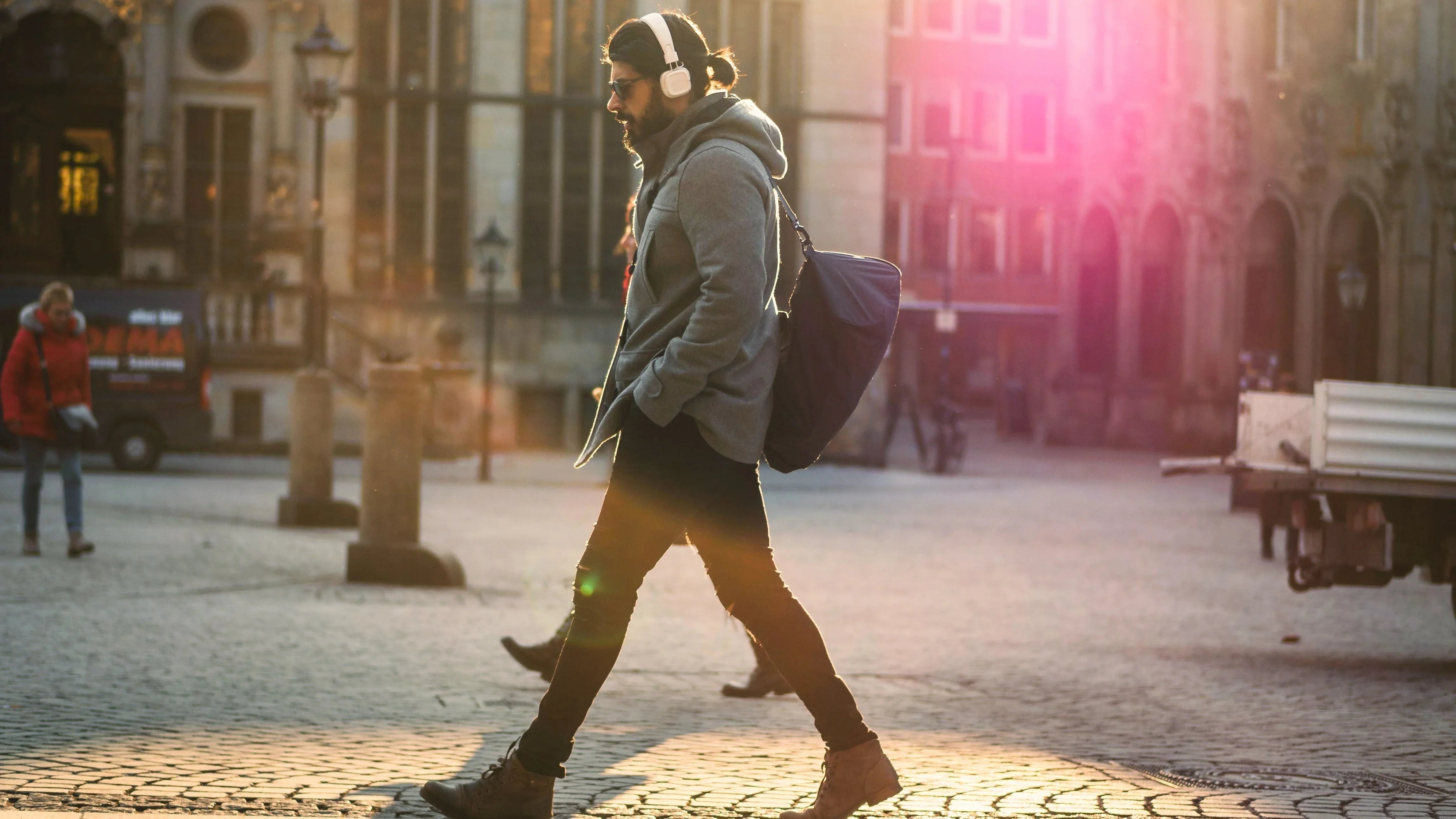 Man walking on cobblestone street wearing white wireless headphones, enjoying immersive sound outdoors