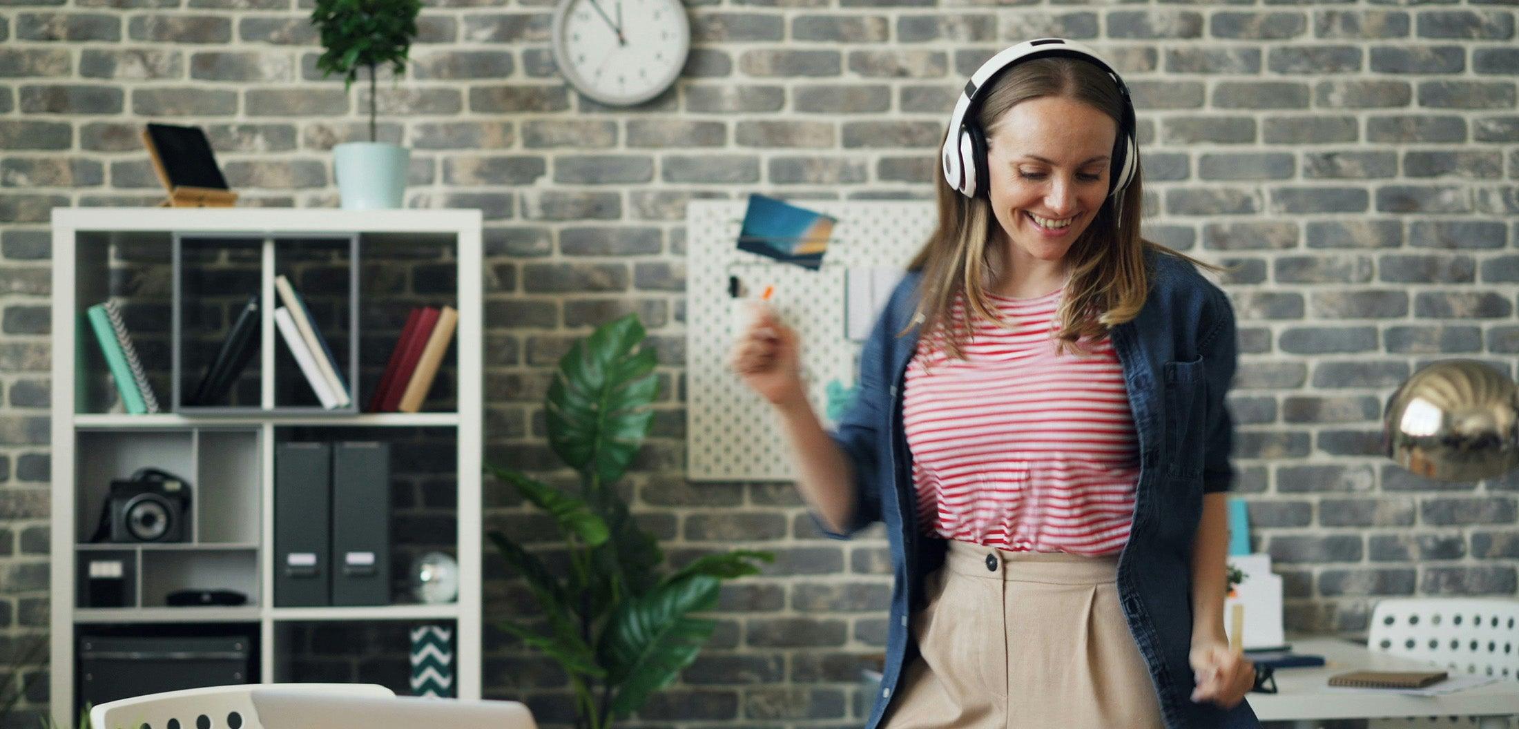 Woman dancing with wireless headphones in modern office, enjoying immersive Bluetooth audio experience