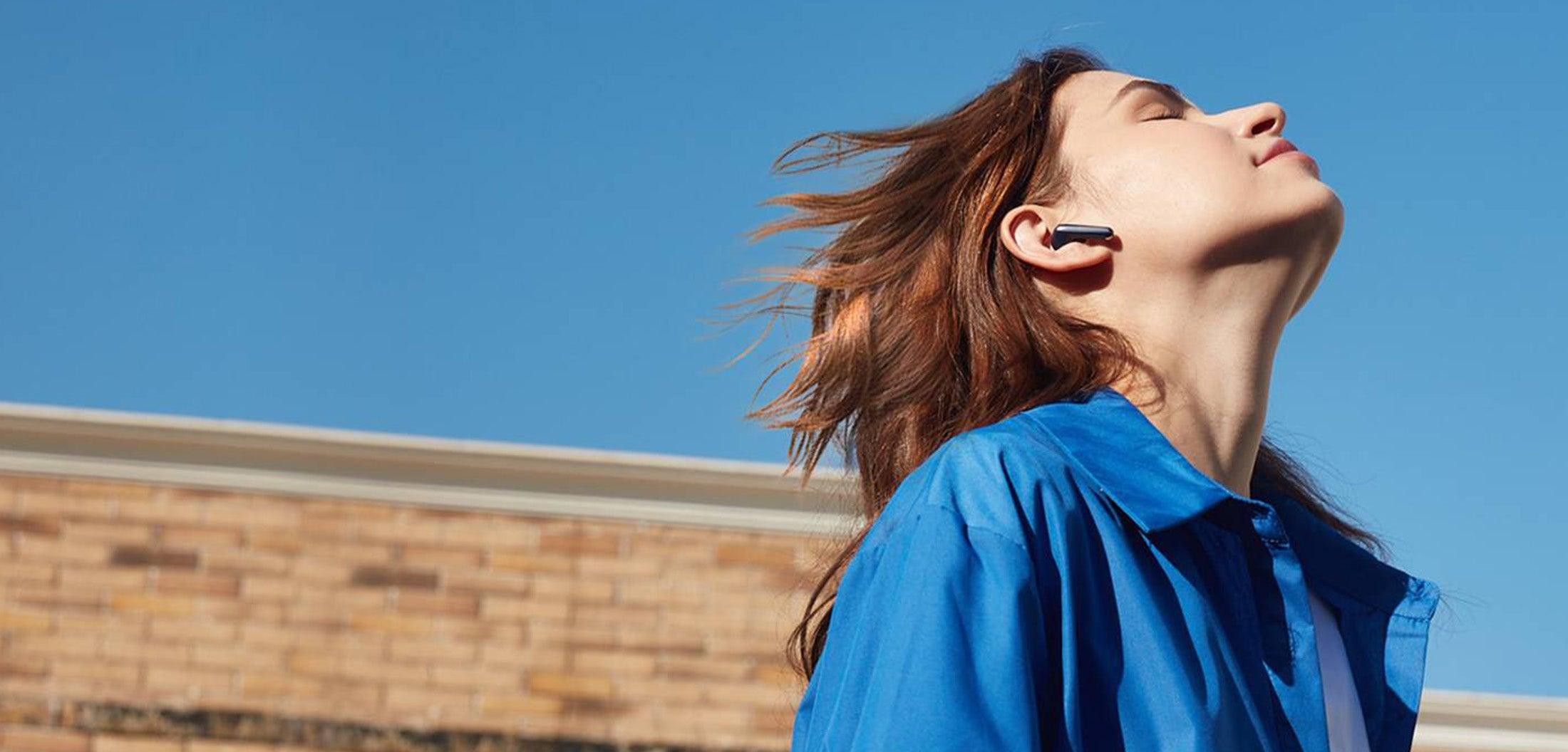 Woman enjoying music with wireless earbuds under blue sky, perfect for iOS and Android