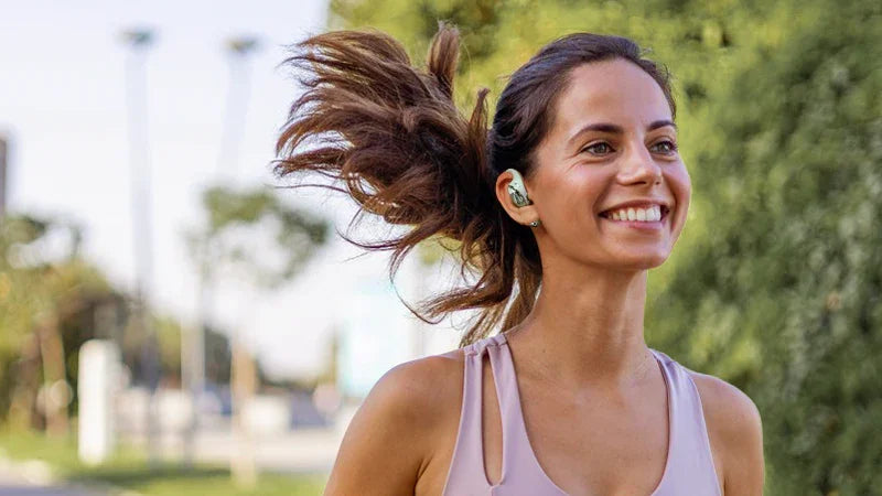 Woman jogging outdoors wearing wireless earbuds, enjoying music during workout