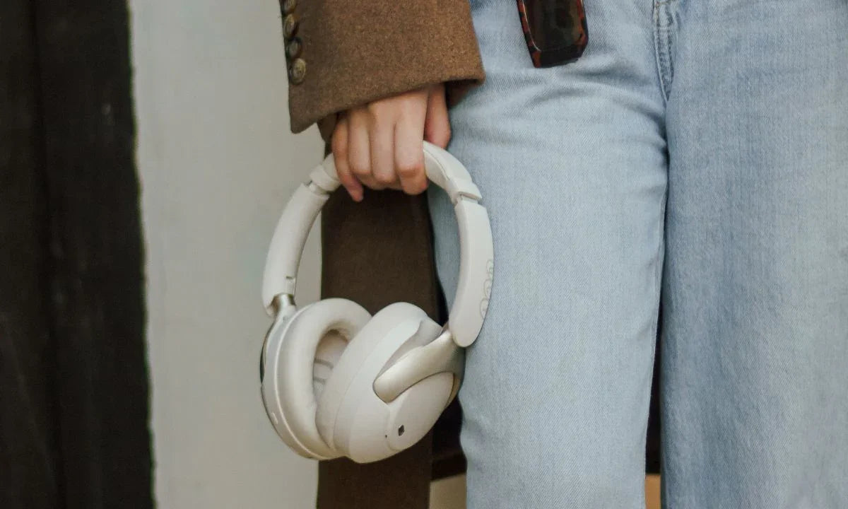 White wireless over-ear headphones held by person in jeans and coat