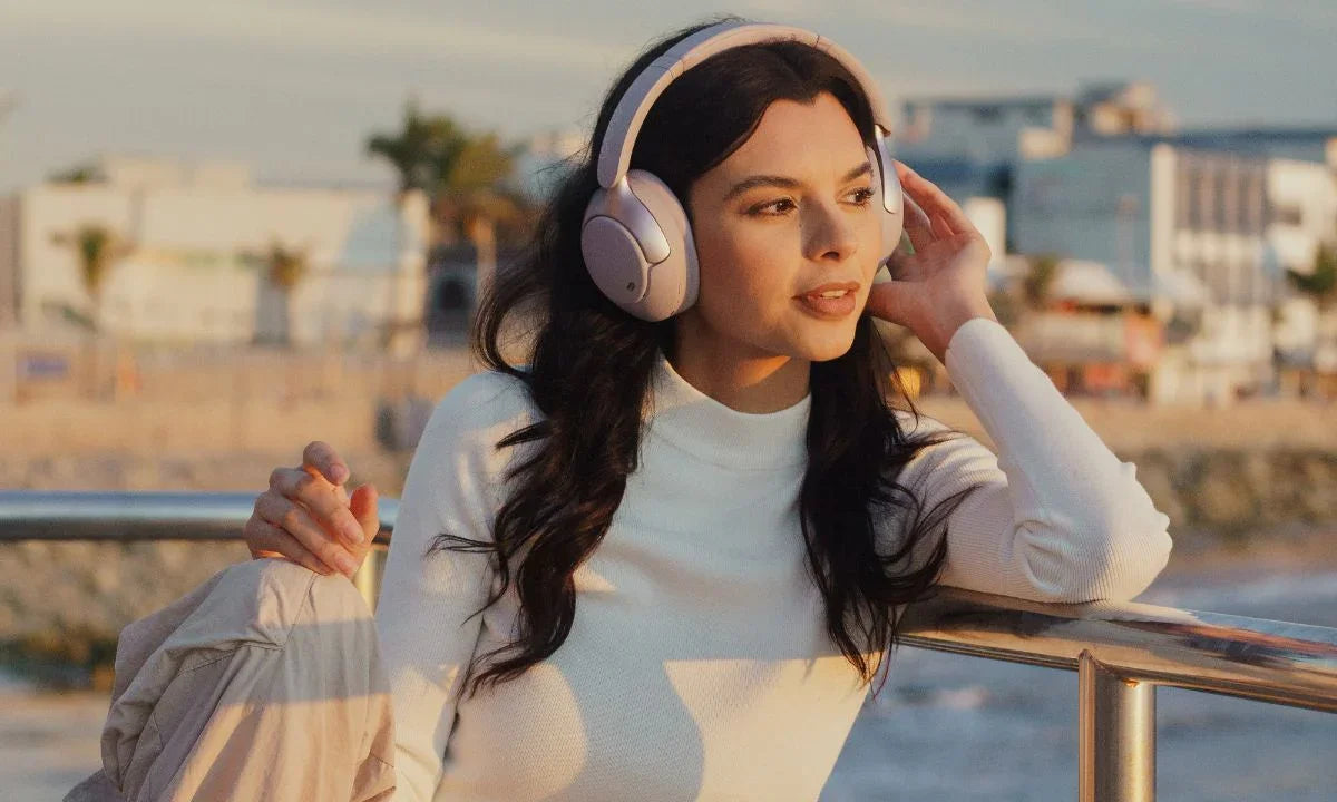 Woman wearing wireless over-ear headphones by waterfront, enjoying immersive audio experience