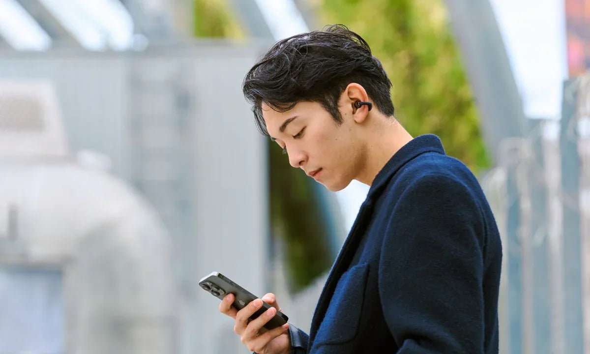 Man using wireless earbuds with smartphone, enjoying Bluetooth audio outdoors