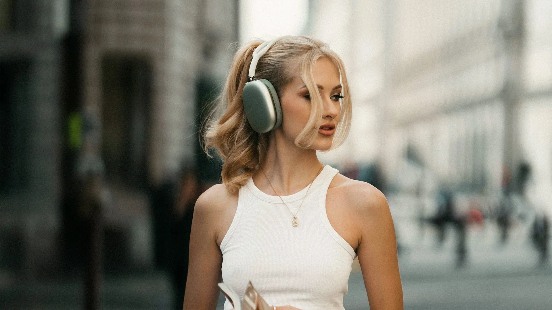 Woman wearing wireless over-ear headphones on city street, enjoying premium Bluetooth audio