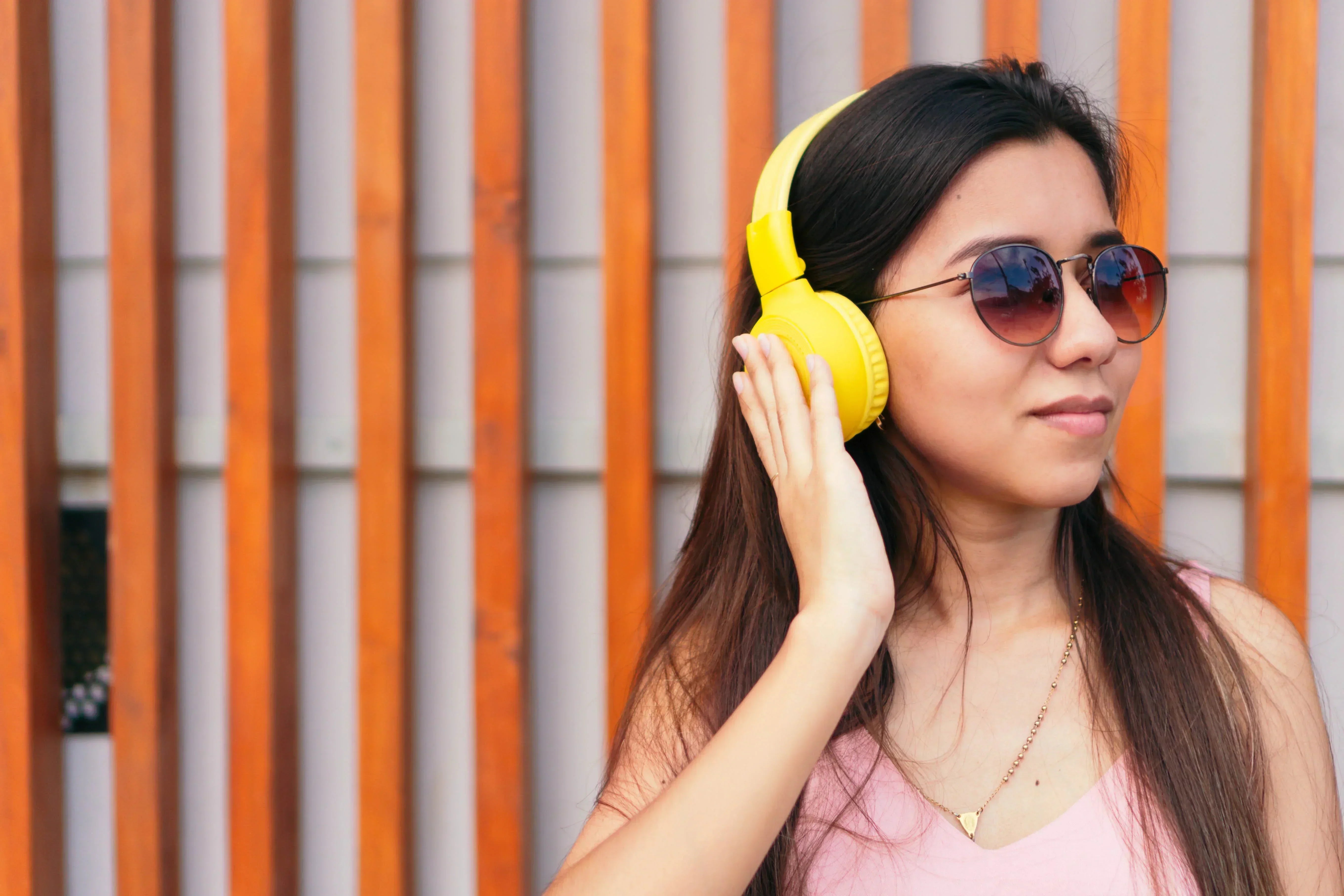 Woman wearing yellow wireless headphones and sunglasses, enjoying music outdoors