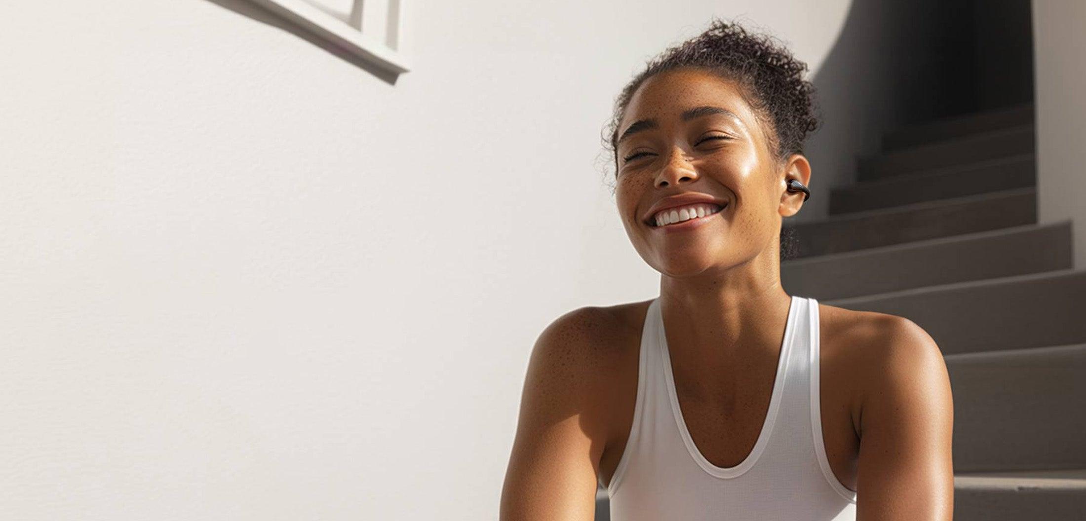 Woman smiling with wireless earbuds, enjoying music outdoors
