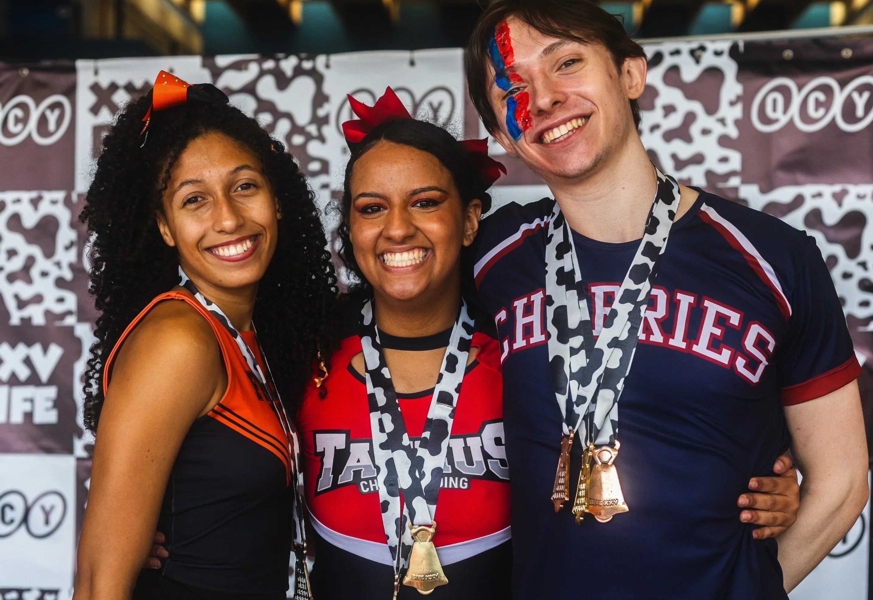 Three smiling athletes in team jerseys with medals, celebrating at a QCY-sponsored event.