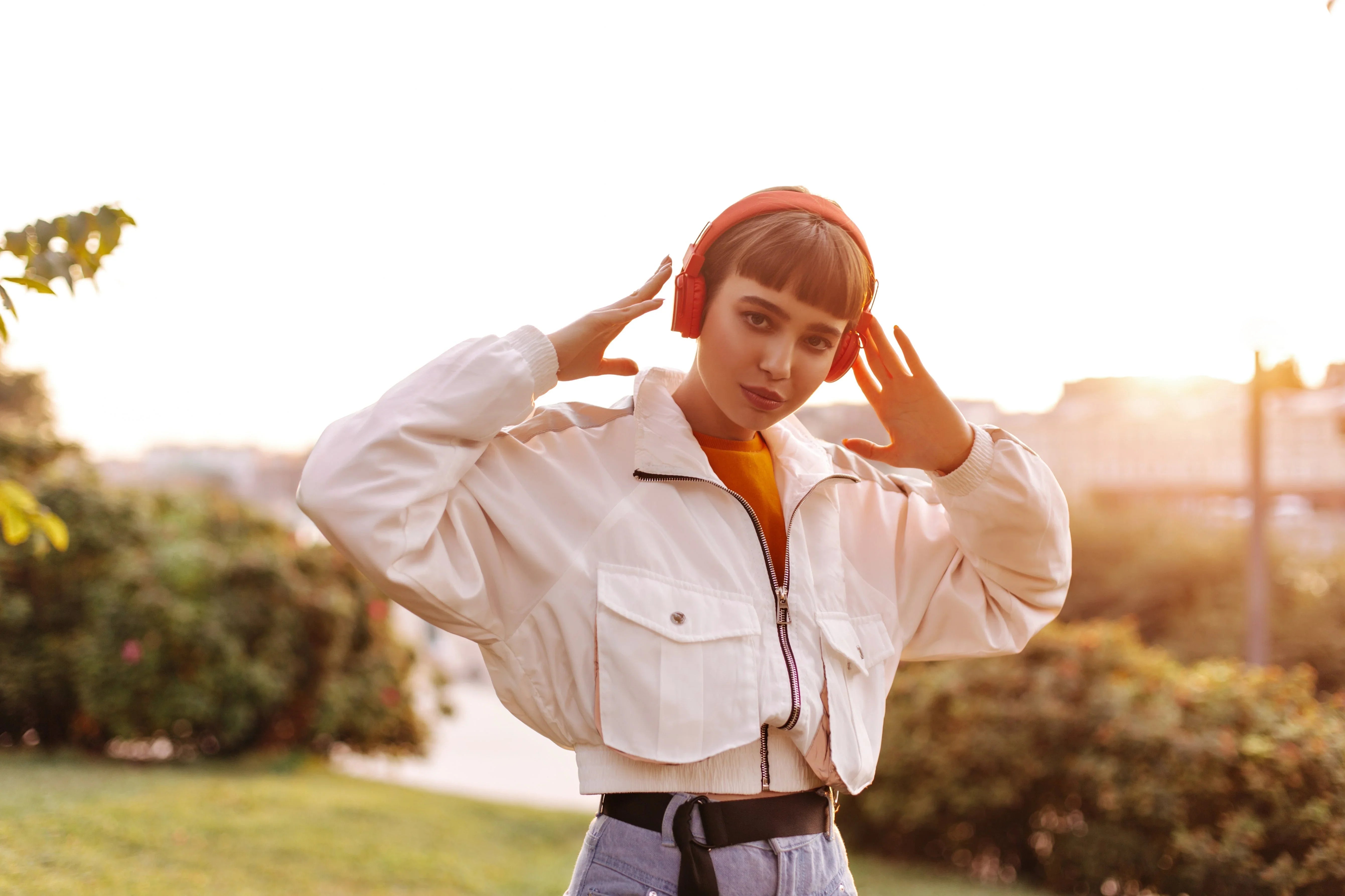 Woman wearing red wireless headphones outdoors, enjoying immersive sound in sunset light