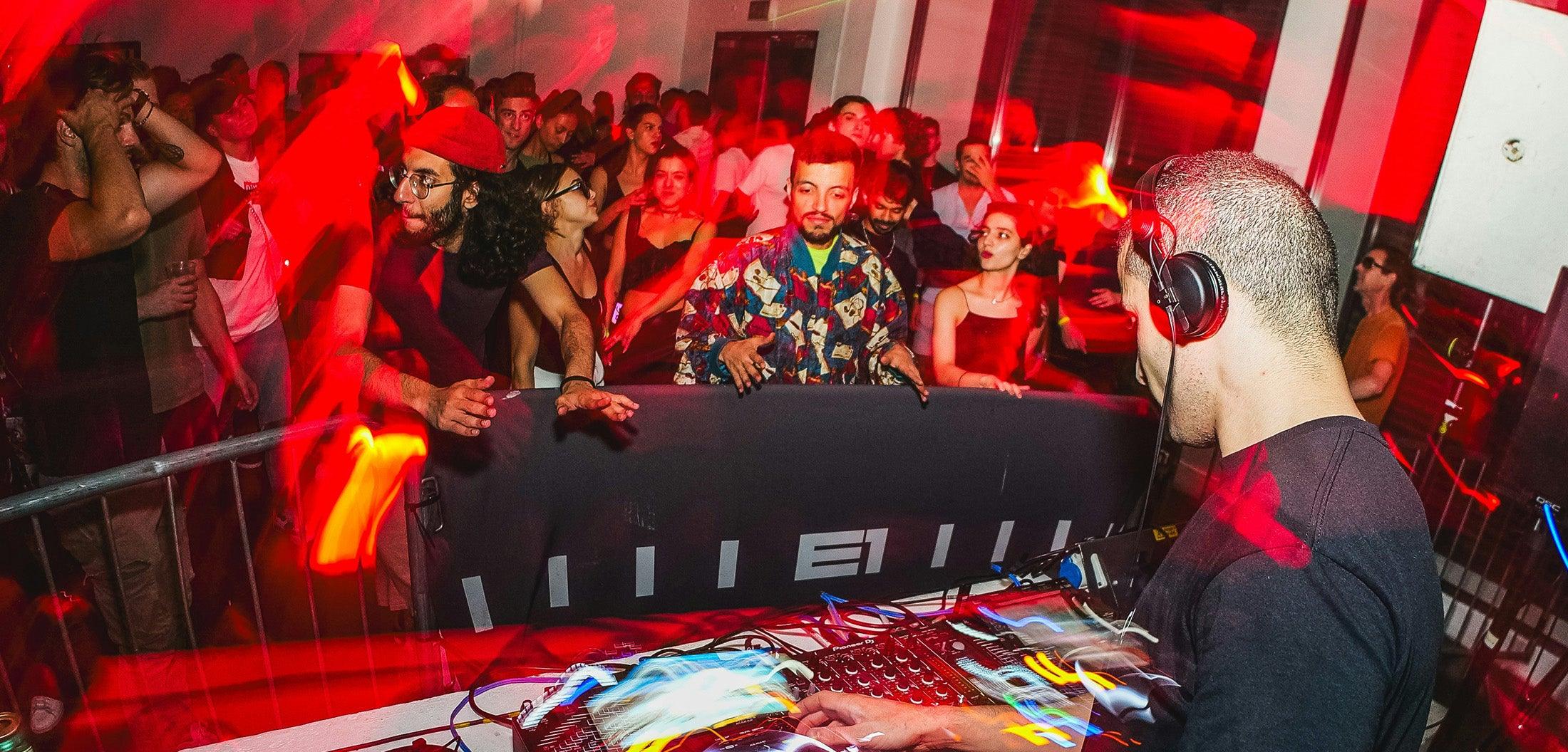 DJ mixing music with wireless headphones at a vibrant red-lit nightclub party