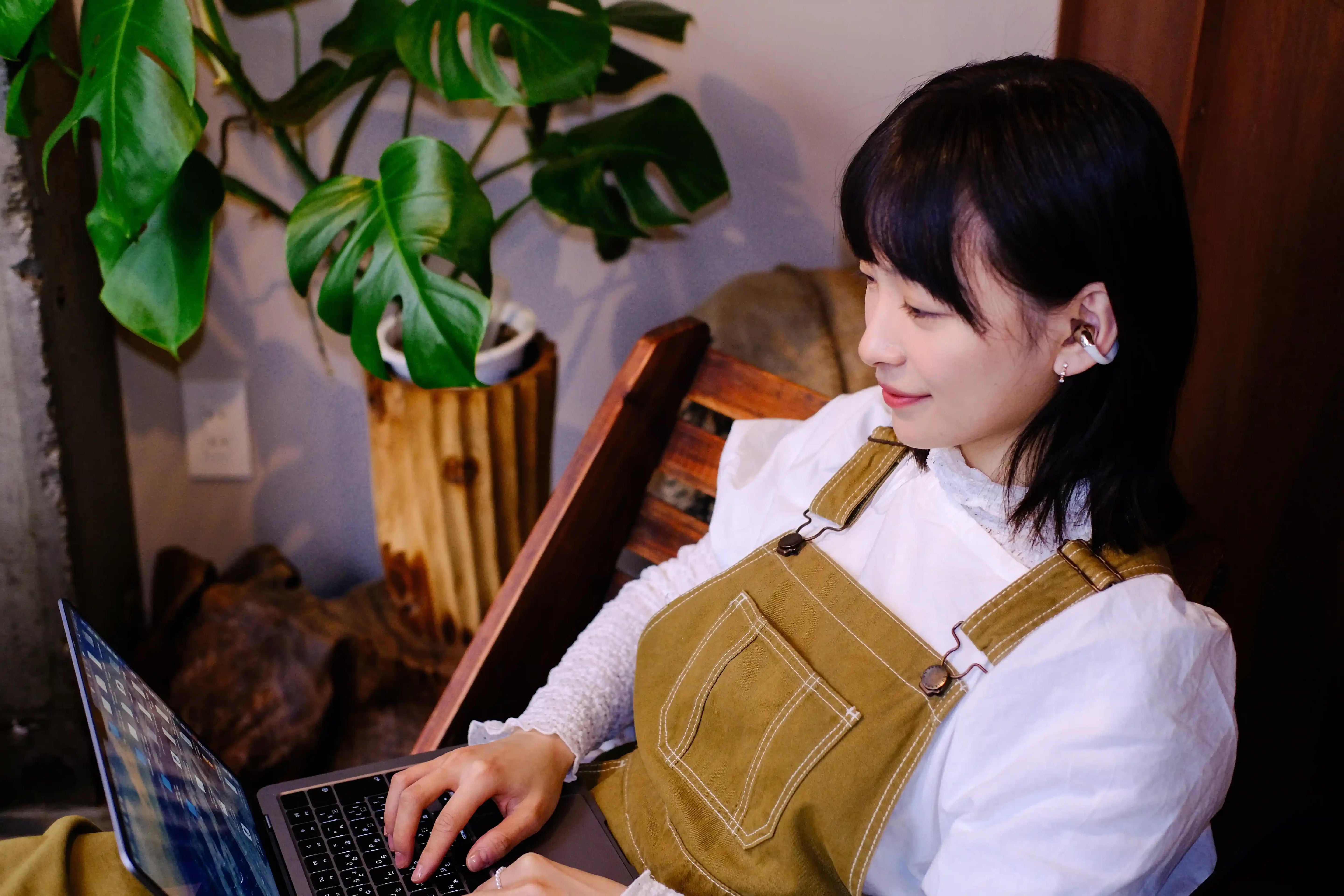 Woman using wireless earbuds while typing on laptop, enjoying immersive audio experience