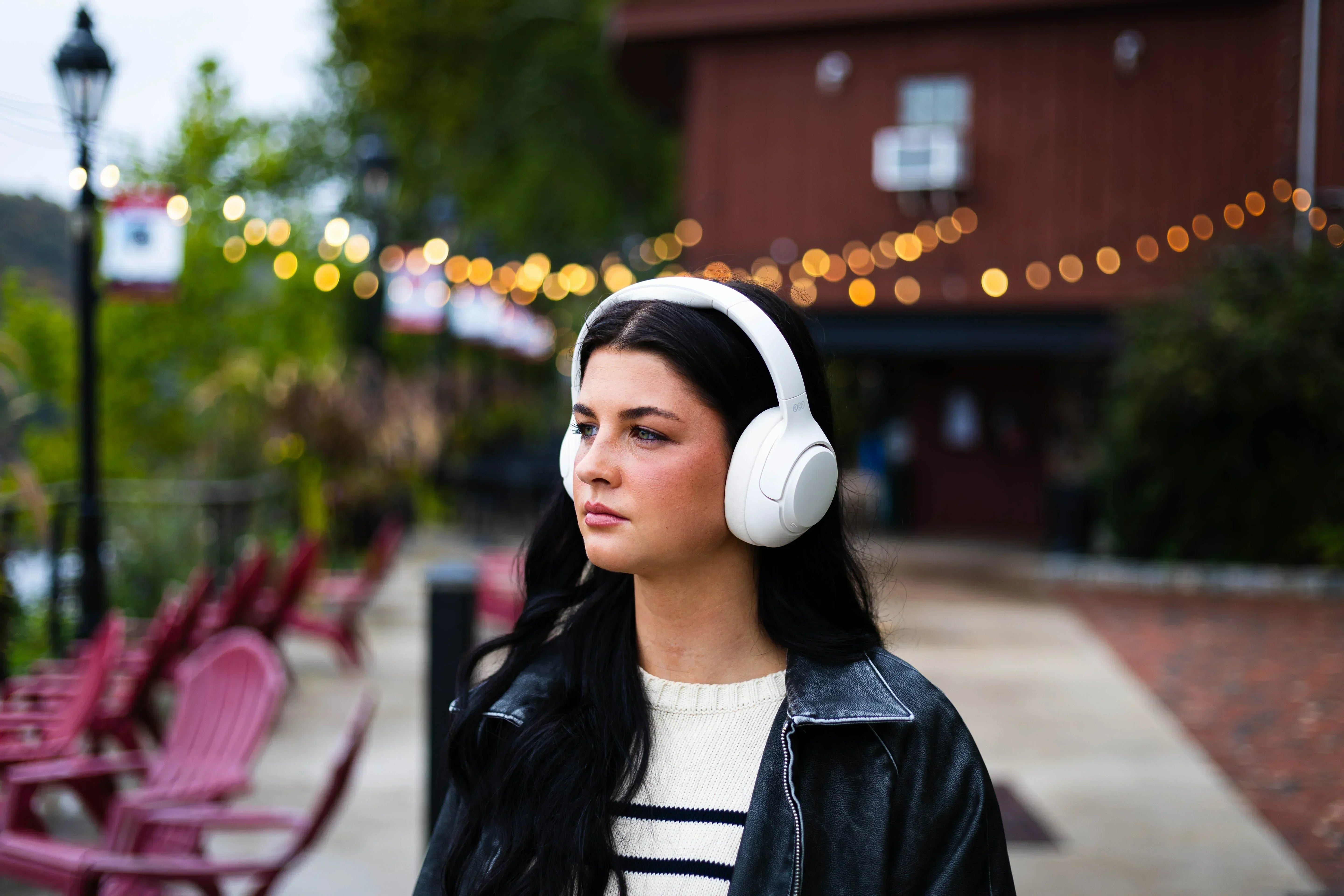 Woman wearing white wireless headphones outdoors with string lights in background