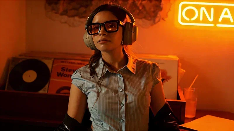 Woman wearing wireless over-ear headphones, listening to music in cozy room with vinyl records and neon light
