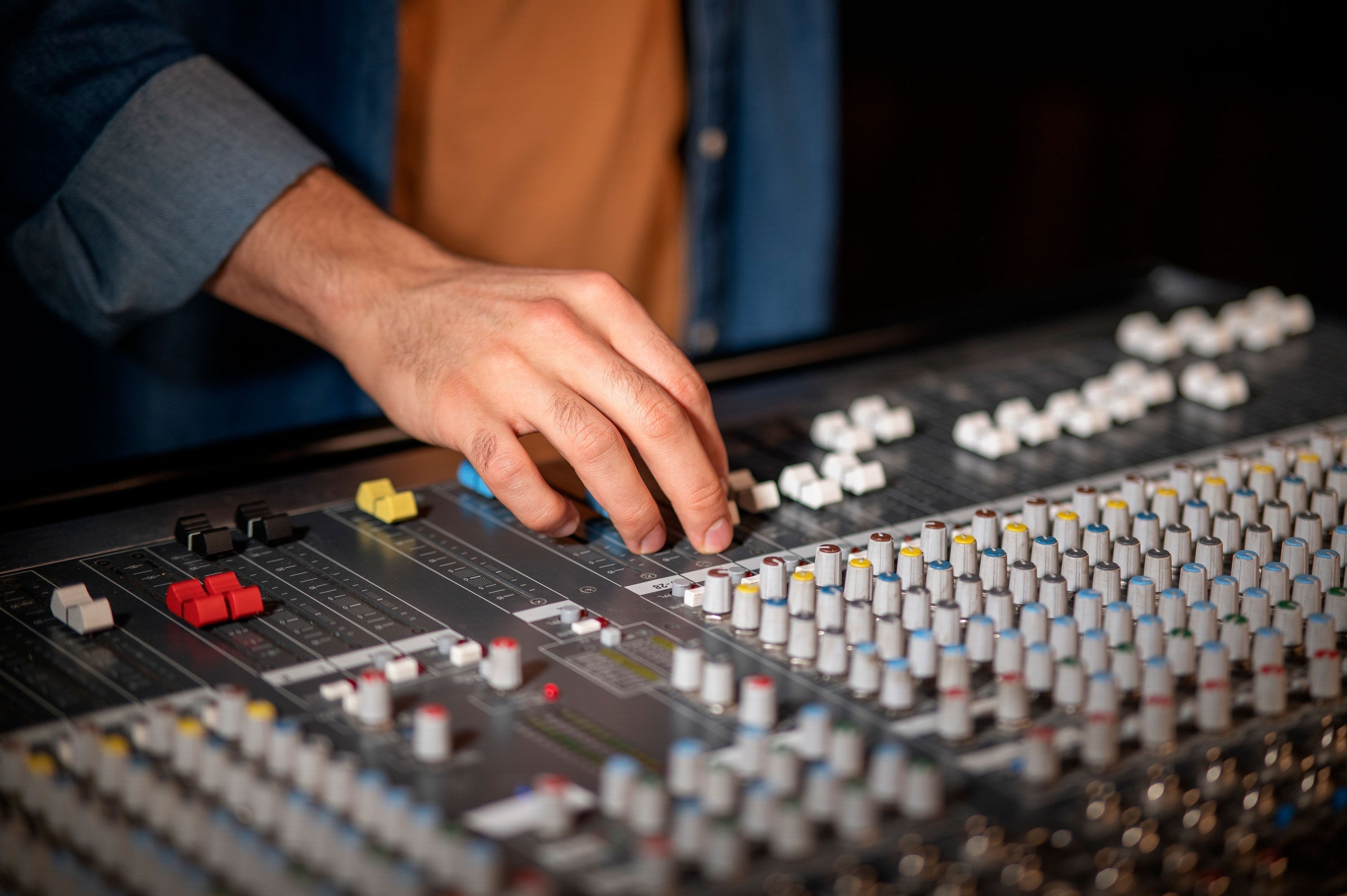 Audio engineer adjusting faders on a professional mixing console for studio sound production
