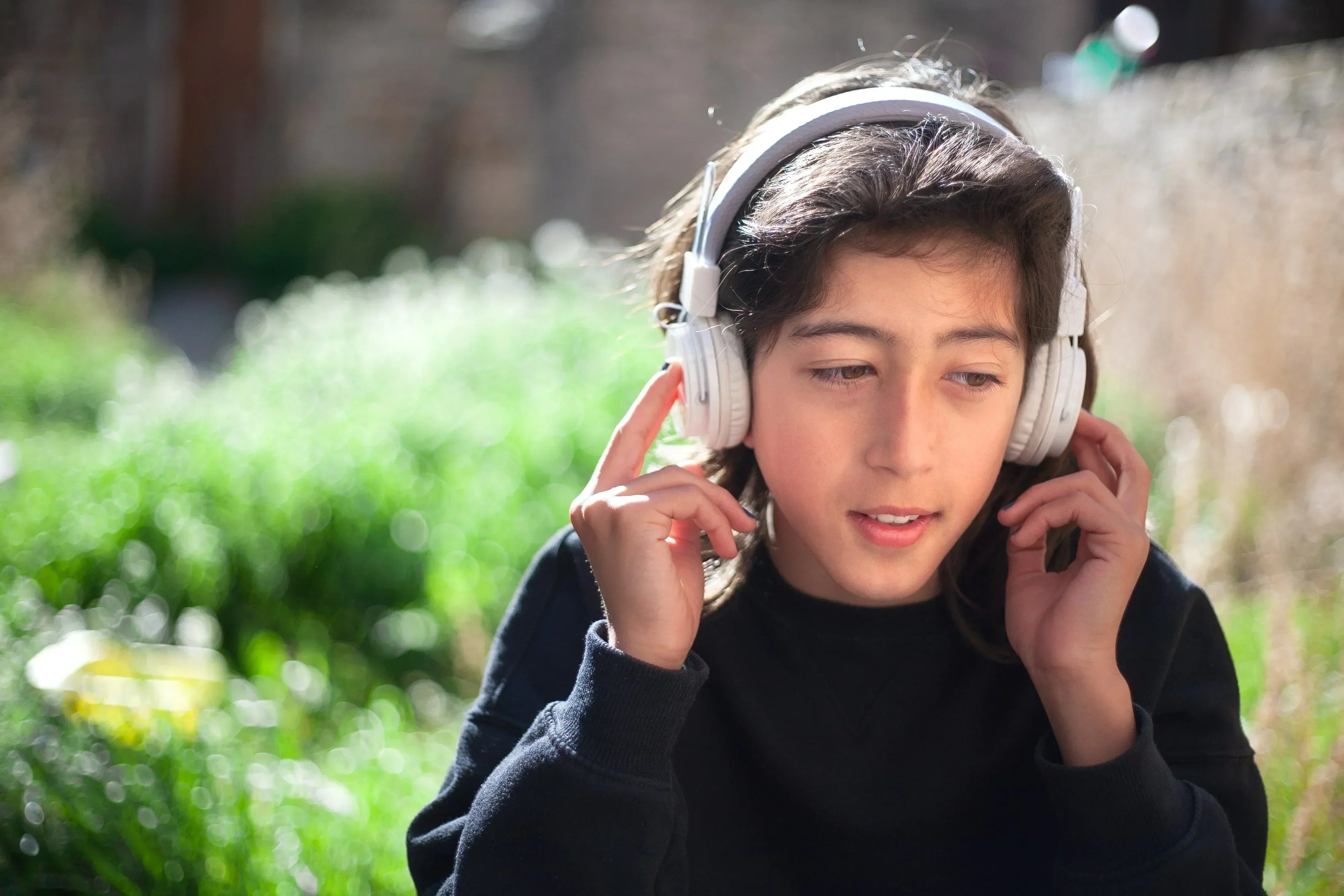 Teen wearing white wireless headphones outdoors, enjoying immersive audio experience in sunny garden