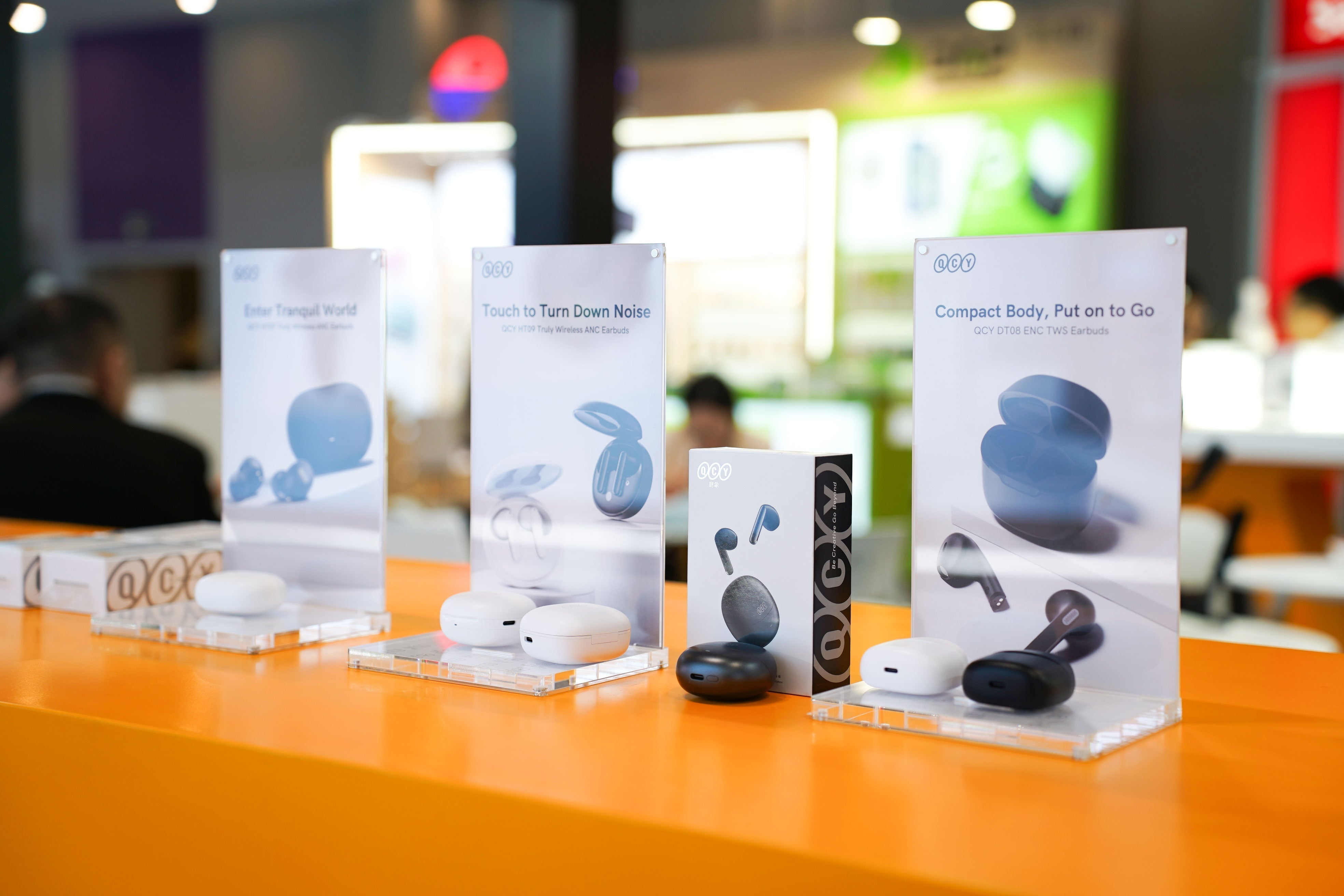 QCY wireless earbuds display with ANC features, compact design, and touch controls on orange retail table