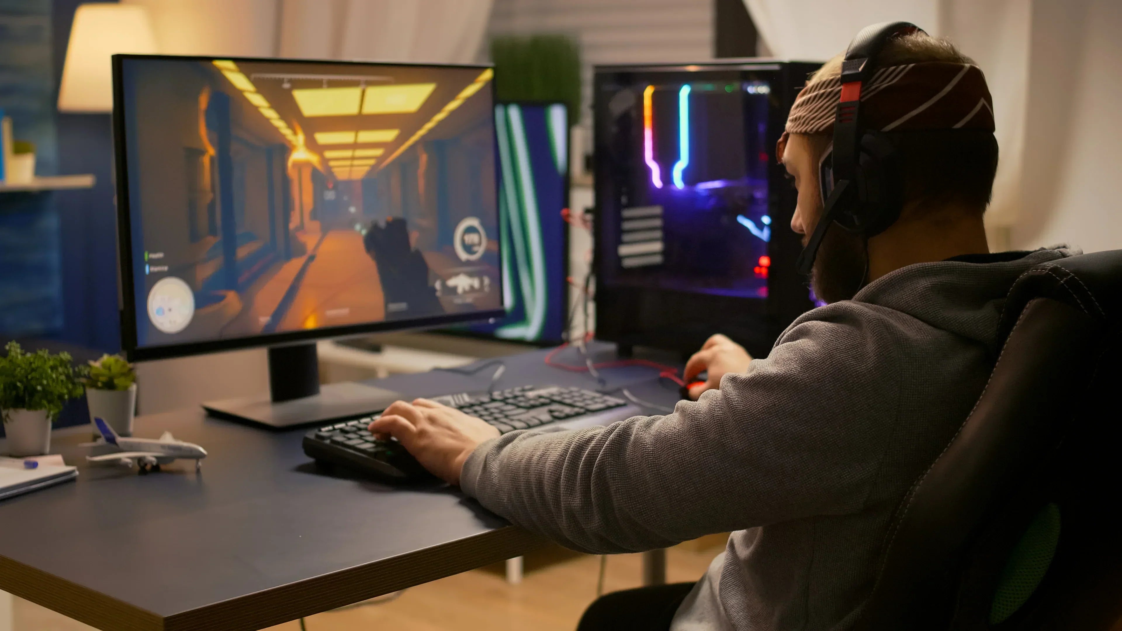 Gamer wearing wireless gaming headset, playing first-person shooter on PC with RGB-lit setup