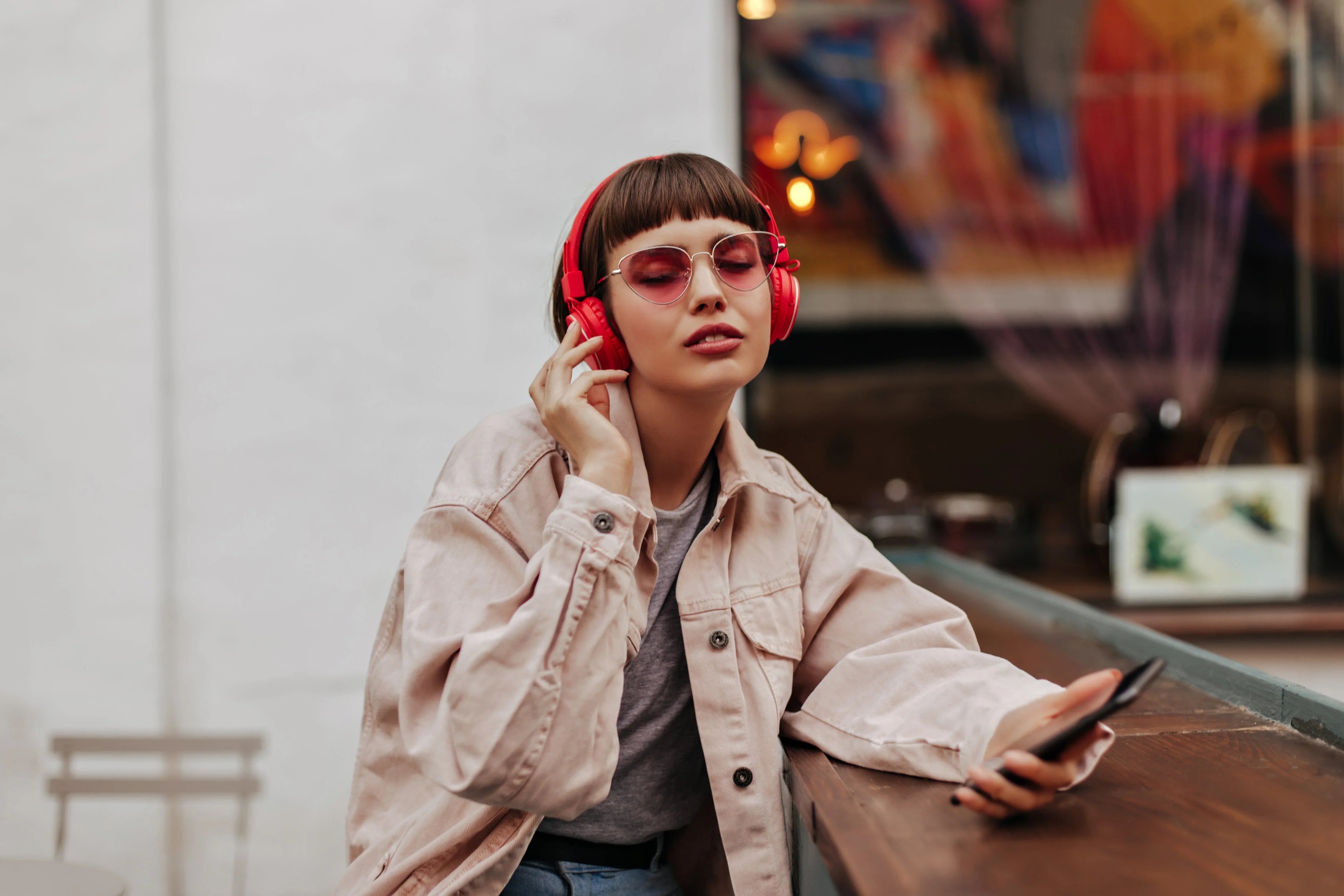 Woman wearing red wireless headphones, enjoying music at a cafe with smartphone in hand