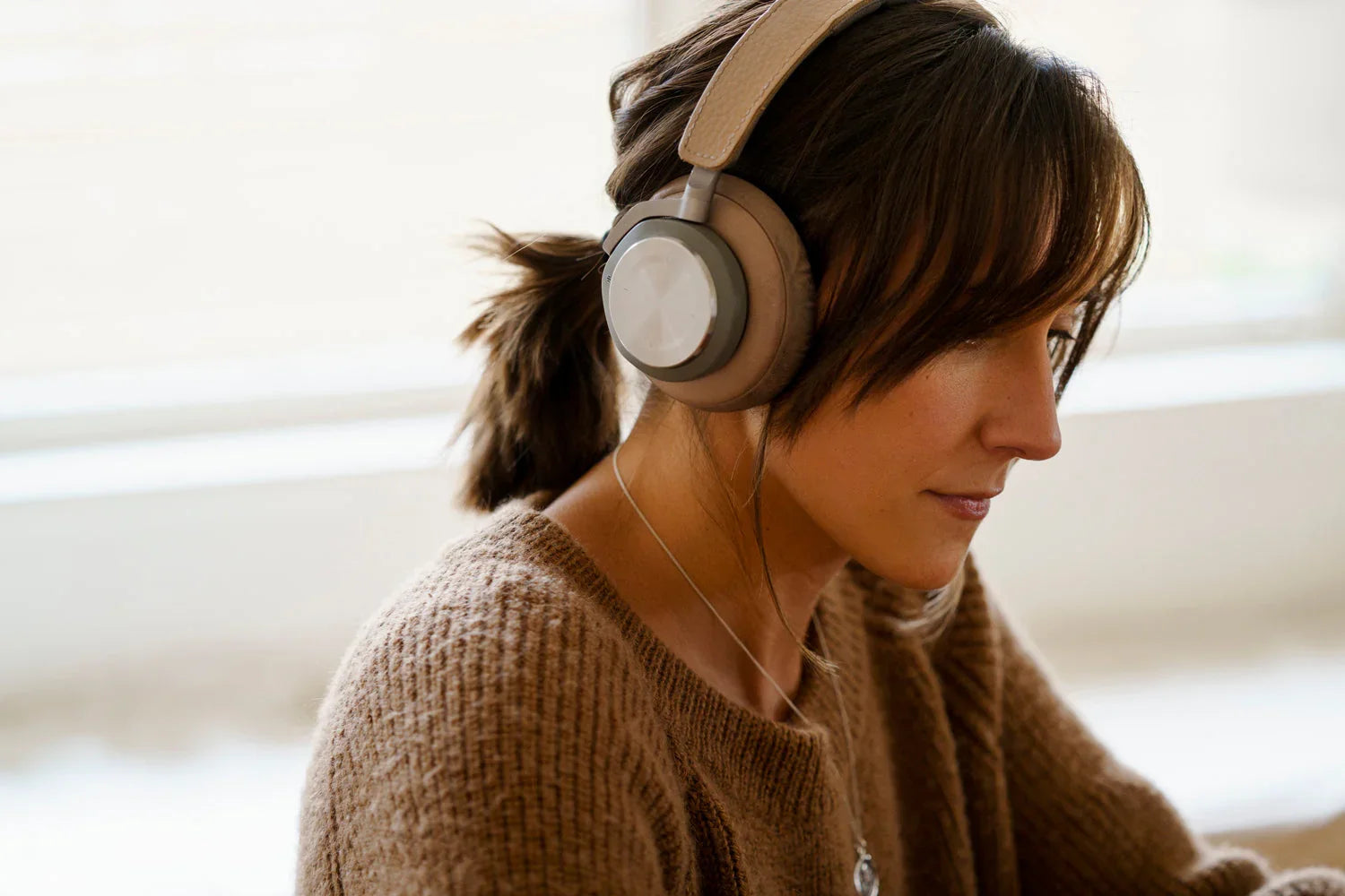 Woman wearing beige over-ear wireless headphones, enjoying immersive sound at home
