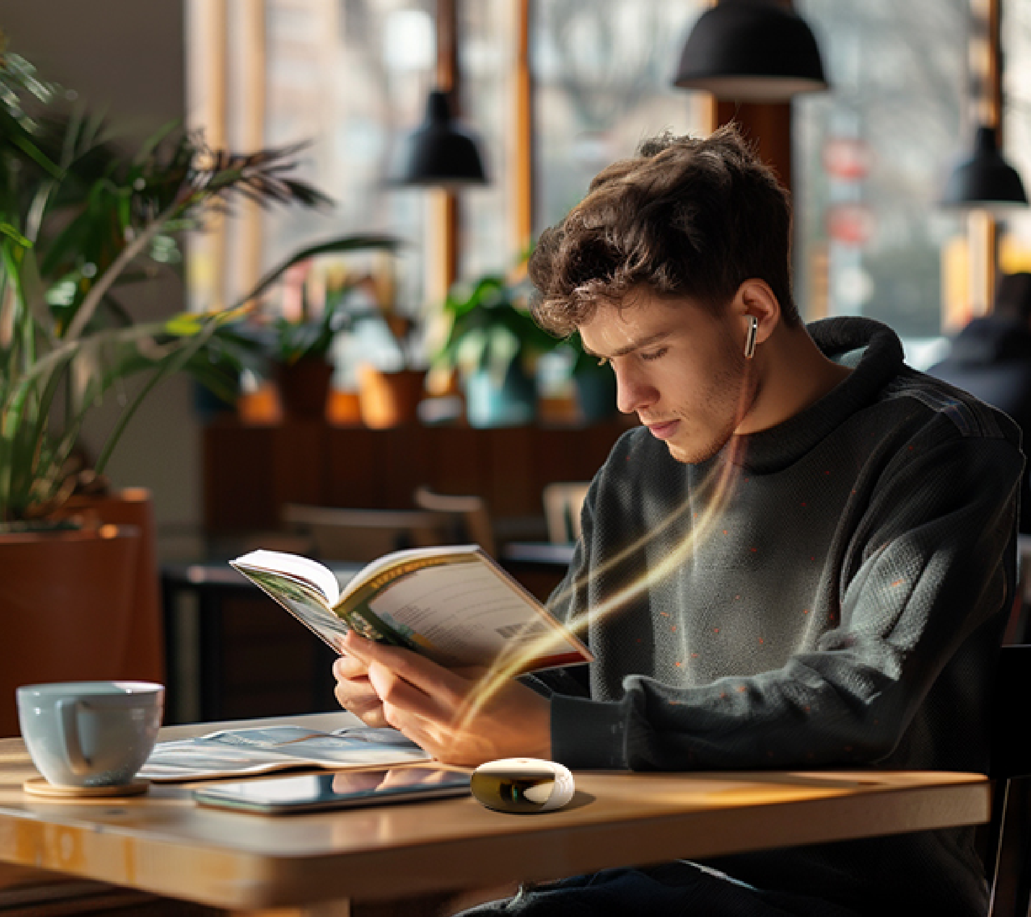 Young man reading book in cozy cafe with coffee cup and plants