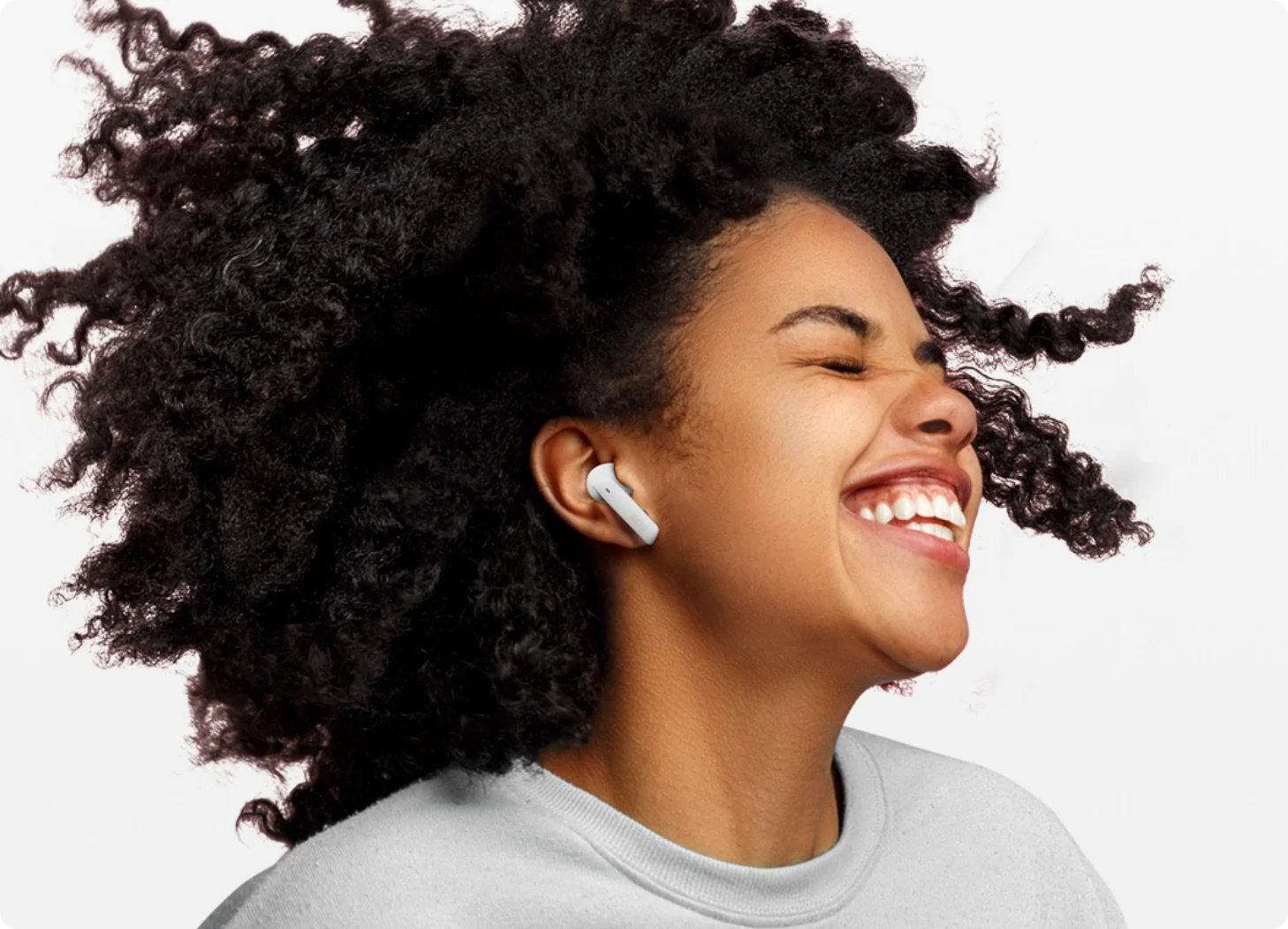 Woman with curly hair smiling wearing white wireless earbuds
