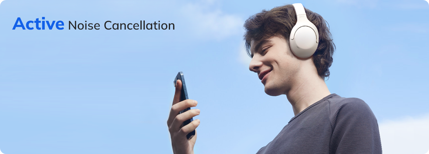 Man wearing white active noise cancellation headphones, smiling while using smartphone outdoors against blue sky.