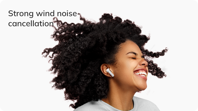 Woman with curly hair smiling outdoors wearing white wireless earbuds featuring strong wind noise cancellation technology.