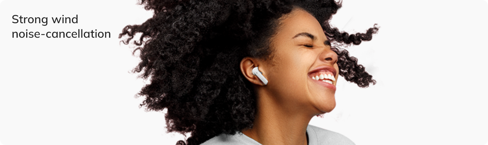 Woman with curly hair wearing white wireless earbuds, strong wind noise-cancellation feature highlighted.